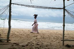 Quiet Beach Bar Grand Bassam, woman with head load walking past on beach, raging sea behind, Cote d'Ivoire, Ivory Coast.