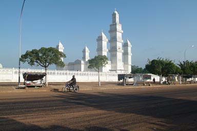 Yamoussoukro, white mosque, moped on black tared road in front.