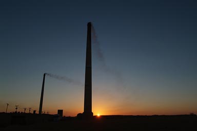 Brick burning chimneys, Dakhla oasis town, sunrise behind, southern Egypt.