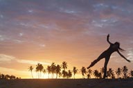 Sunset dance on beach, palm trees in red sky, girl dancing on beach.