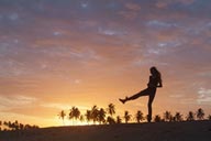 Sunset dance on beach, palm trees in red sky, girl dancing on beach.