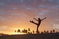 Sunset dance on beach, palm trees in red sky, girl dancing on beach.