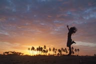 Sunset dance on beach, palm trees in red sky, girl dancing on beach.