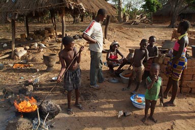 Roasting cashews, African village in the South of Guinea Bissau, African Family, boy steering in a bowl lit aflame, cashew broth is blazing, burning off the flesh surrounding the nut, the oil evaporates and burns off as well.