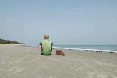 Me, white European, red short, green torn Langnesse, T-shirt, hat, back to the camera, on south beach of Bubaque called Brousse, Arquipelago dos Bijagos. Islands. Guinea Bissau.