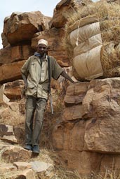 Dogon hunter and rifel, his straw load, on descent from cliffs