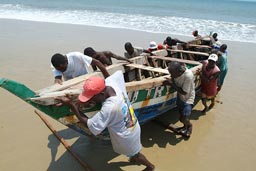 Fishermen push their boat up shore. Sierra Leone.