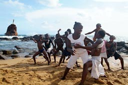 children pose on beach, shipwreck on rocks in back, Buchanan, Liberia.