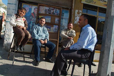 Friendly Syrian men and a boy sitting, laughing in street.
