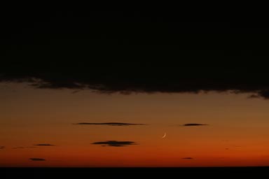 New new-moon, on orange sky, black clouds above and below.