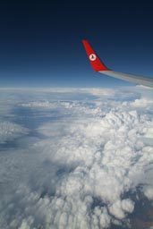 Wing of Turkish Airlines plane white clouds against blue sky.