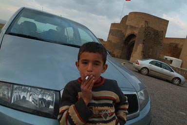 Boy on parking Ani, leans on car bonnet and smokes cigarette. Ani's city walls in back.