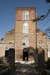 Front of brick St. John's Cathedral in Belize City. A sign on entry says: A contribution is requested from visitors!