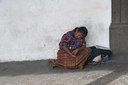 Indigenous lady, Maya, sleeps leaned on house wall, street in Antigua, Guatemala.