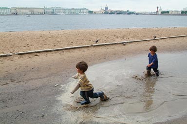 Twins in St. Petersburg, gumboots in puddle, beach and waterfront in back.
