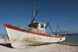 Morning beach in Santa Clara, white and red fishing boat against blue sky.
