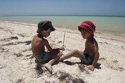 Boys with hat sit on beach far, white and untouched.