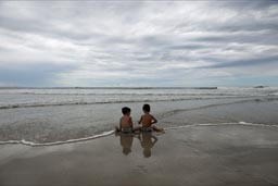 Boys sit on beach and discuss, looking out on ocean.