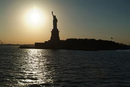 Liberty island and statue, silhouette against sun.