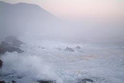 Evening, coastal cliffs vanish in white haze.