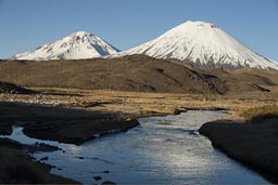 Volcanoes Pomerape and Parinacota over a blue stream high up, northern Chile.