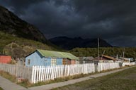 Dark clouds, low evening sun lights wooden houses and white fence in Villa O'Higgins.