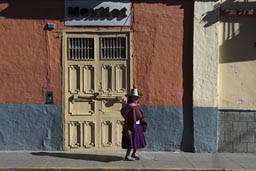 Indigenous woman in dress and hat walks a morning lighted street in Cajamarca, Peru. 