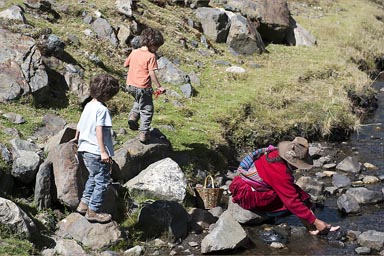 Indigenous Andean woman washes her shoes and feeet in cold Cordillera Blanca stream, my boys watch, Peru.